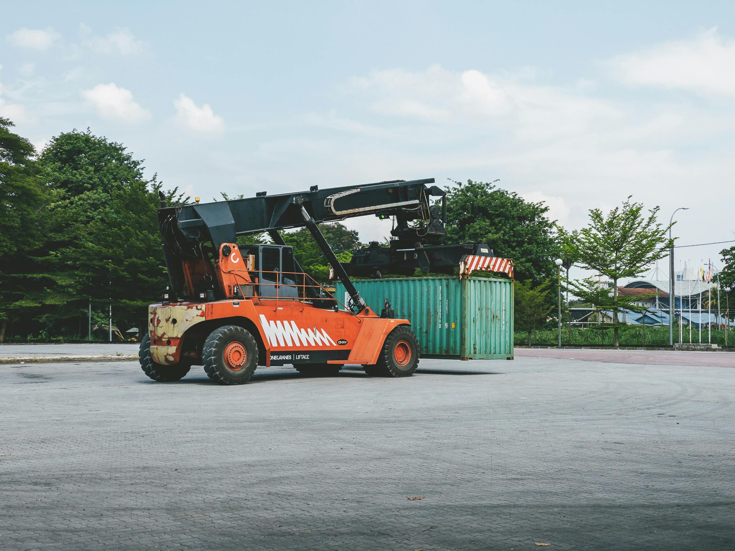 A container handler lifts a cargo container at an outdoor industrial port in Ipoh, Malaysia.
